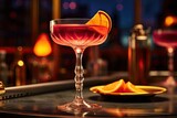 Fototapeta  - A bar setting with a closeup view of a glass filled with a cosmopolitan cocktail, garnished with a slice of orange.