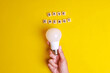 Save Energy words written on wooden blocks with hand holding white light bulb on yellow background. Concept of saving energy by using LED lightbulb