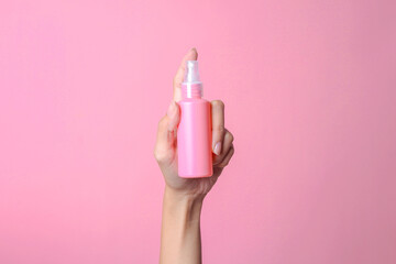 Woman hand holding blank cosmetic spray bottle for mockup isolated over pink background