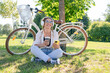 © Julija - Close up of happy young girl listening to music with mobile phone and earphones while sitting at the park with a bicycle. Lifestyle. Relax, nature concept