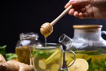 Wall Mural - woman pours honey in a cup with natural organic herbal tea and glass teapot on a wooden table