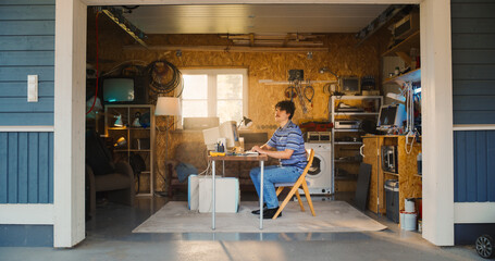 Leinwandbilder - Caucasian Male Software Engineer Entering Retro Garage And Sitting At His Work Desk With Old Desktop Computer. Focused Man Starting Software Startup Company In Nineties, Working On Digital Product.