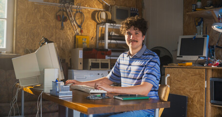 Leinwandbilder - Caucasian Male Software Engineer Programming On Old Desktop Computer In Retro Garage, Looking At Camera And Smiling. Man Starting an Innovative Startup Company In Nineties. Nostalgia Concept.