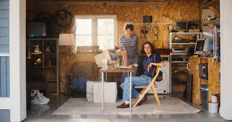 Two Caucasian Male Tech Startup Founders Using Old Desktop Computer In Retro Garage, Looking At Camera And Smiling. Programmer And UX Designer Starting Internet Business In Nineties. Nostalgia Concept