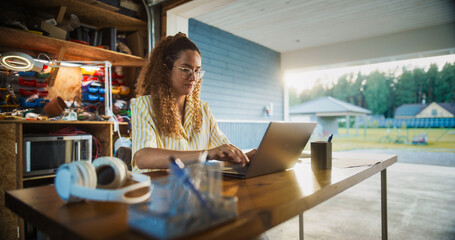 Fototapete - Happy Hispanic Woman Using Laptop Computer In Opened Garage. Successful Female Digital Entrepreneur Running An E-commerce Startup From Home, Checking Emails, Filling Online Orders, Researching Market.