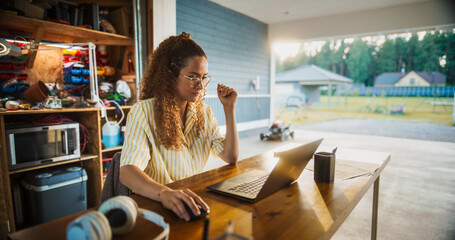 Poster - Young Hispanic Female Software Engineer Programming On Laptop Computer In Opened Garage. Woman Running A Startup With Innovative SaaS Solution For Businesses. Developer Writing Code, Optimizing System