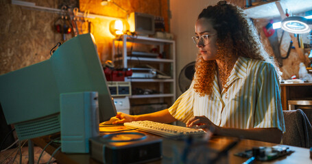 Leinwandbilder - Hispanic Female Engineer Using Old Desktop Computer In Nineties Retro Garage In The Evening. Intelligent Woman Programming, Working On Innovative Portable Device, Starting Tech Startup Company.