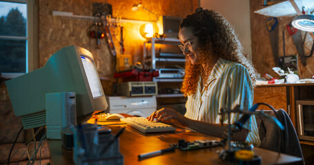 Leinwandbilder - Hispanic Female Engineer Using Old Desktop Computer In Nineties Retro Garage In The Evening. Intelligent Woman Writing Code, Working On Innovative Portable Device, Starting Tech Startup Company.