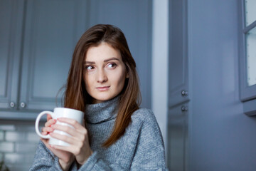 Wall Mural - young woman in a warm sweater with a mug in her hand, concept of the morning of a new day