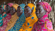 Gruppe von erwachsenen afrikanischen Frauen in traditioneller Kleidung, die nebeneinander sitzen und jemandem zuhören 