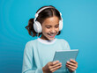 Portrait of girl wearing headphones and holding tablet on blue background.