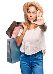 Wall Mural - Beautiful caucasian woman holding shopping bags with open hand doing stop sign with serious and confident expression, defense gesture