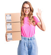 © Krakenimages.com - Young caucasian woman with blond hair holding delivery package doing ok sign with fingers, smiling friendly gesturing excellent symbol