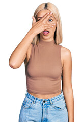 Wall Mural - Beautiful young blonde woman wearing casual style with sleeveless shirt peeking in shock covering face and eyes with hand, looking through fingers with embarrassed expression.