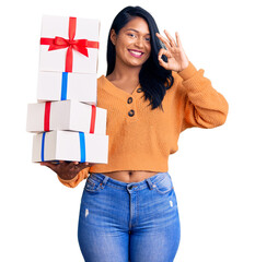 Poster - Hispanic woman with long hair holding gifts doing ok sign with fingers, smiling friendly gesturing excellent symbol