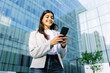 © Xavier Lorenzo - Successful young adult businesswoman using mobile cell phone outside over business building office. Technology lifestyle and business concept