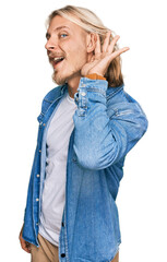 Poster - Caucasian man with blond long hair wearing casual denim jacket smiling with hand over ear listening an hearing to rumor or gossip. deafness concept.