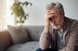 © Irene - Middle-aged man with a beard, sitting on the sofa with his hand on his head, eyes closed, indicating a headache and fatigue, stress, and anxiety