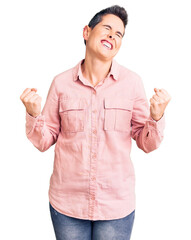 Young woman with short hair wearing casual clothes very happy and excited doing winner gesture with arms raised, smiling and screaming for success. celebration concept.