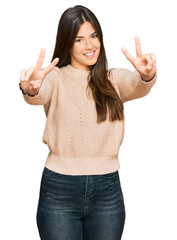 Canvas Print - Young brunette woman wearing casual winter sweater smiling with tongue out showing fingers of both hands doing victory sign. number two.