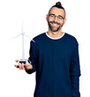 Hispanic man with ponytail holding solar windmill for renewable electricity looking positive and happy standing and smiling with a confident smile showing teeth