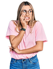 Wall Mural - Hispanic young woman wearing casual t shirt and glasses looking stressed and nervous with hands on mouth biting nails. anxiety problem.