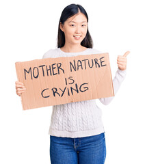 Sticker - Young beautiful chinese woman holding mother nature is crying cardboard banner smiling happy and positive, thumb up doing excellent and approval sign