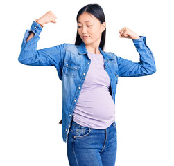 Poster - Young beautiful chinese woman pregnant expecting baby showing arms muscles smiling proud. fitness concept.