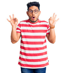 Wall Mural - Handsome latin american young man wearing casual clothes and glasses looking surprised and shocked doing ok approval symbol with fingers. crazy expression