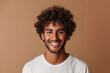 Portrait of merry positive curly haired Hindu man smiles pleasantly being in good mood dressed in casual t shirt looks directly at camera isolated over brown background