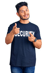 Wall Mural - Handsome latin american young man wearing security t shirt pointing fingers to camera with happy and funny face. good energy and vibes.