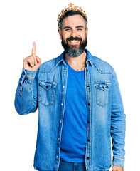 Wall Mural - Hispanic man with beard wearing king crown pointing finger up with successful idea. exited and happy. number one.