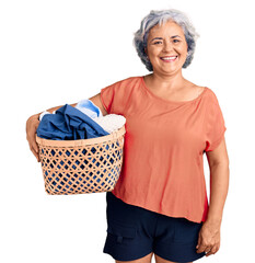 Poster - Senior woman with gray hair holding laundry basket looking positive and happy standing and smiling with a confident smile showing teeth