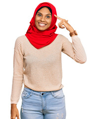 Wall Mural - Young african american woman wearing traditional islamic hijab scarf smiling pointing to head with one finger, great idea or thought, good memory