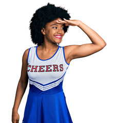 Poster - Young african american woman wearing cheerleader uniform very happy and smiling looking far away with hand over head. searching concept.