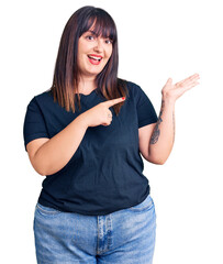 Sticker - Young plus size woman wearing casual clothes amazed and smiling to the camera while presenting with hand and pointing with finger.