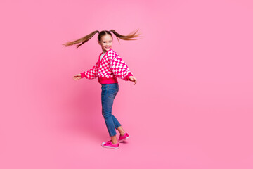 Poster - Full size photo of positive schoolgirl with tails dressed knit cardigan turning around near empty space isolated on pink color background