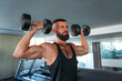 Caucasian man with a hairstyle and a beard trains his arms and shoulders with synchronized lifting of dumbbells