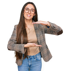 Poster - Young hispanic girl wearing business clothes and glasses gesturing with hands showing big and large size sign, measure symbol. smiling looking at the camera. measuring concept.