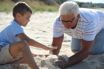 Wall Mural - Cute little boy with grandfather spending time together on sea beach