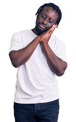 Canvas Print - Young african american man with braids wearing casual white tshirt sleeping tired dreaming and posing with hands together while smiling with closed eyes.