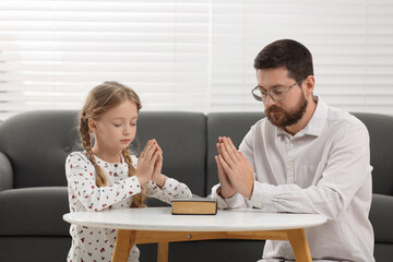 Wall Mural - Girl and her godparent praying over Bible together at table indoors