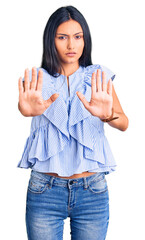 Wall Mural - Young beautiful latin girl wearing casual clothes moving away hands palms showing refusal and denial with afraid and disgusting expression. stop and forbidden.