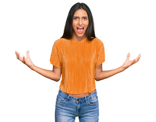 Wall Mural - Young brunette arab woman wearing casual clothes crazy and mad shouting and yelling with aggressive expression and arms raised. frustration concept.