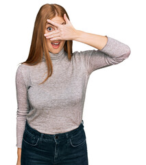 Wall Mural - Young irish woman wearing casual clothes peeking in shock covering face and eyes with hand, looking through fingers with embarrassed expression.