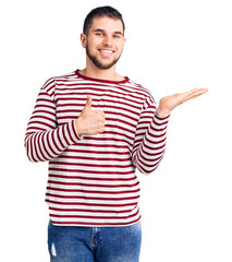 Wall Mural - Young handsome man wearing striped sweater showing palm hand and doing ok gesture with thumbs up, smiling happy and cheerful