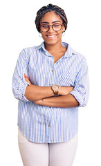 Canvas Print - Young african american woman with braids wearing casual clothes and glasses happy face smiling with crossed arms looking at the camera. positive person.