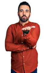 Wall Mural - Young hispanic man with beard wearing casual shirt looking at the camera blowing a kiss with hand on air being lovely and sexy. love expression.