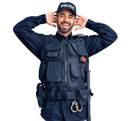 Canvas Print - Young hispanic man wearing police uniform relaxing and stretching, arms and hands behind head and neck smiling happy