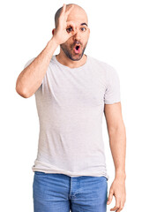 Canvas Print - Young handsome man wearing casual t shirt doing ok gesture shocked with surprised face, eye looking through fingers. unbelieving expression.